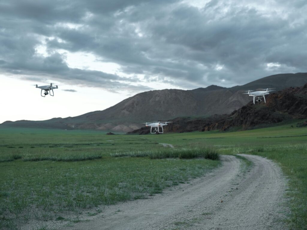Aerial drones hovering over a picturesque landscape with fields and mountains under a cloudy sky.
